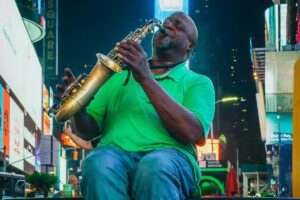 Auf dem Bild ist ein Mann in einer grünen Poloshirt und blauen Jeans zu sehen, der in Times Square eine Saxofonblase spielt. Die bunten Leuchttafeln und der urbane Hintergrund geben der Szene einen unverwechselbaren Flair. Ebenso wie die Musik des Mannes die Menschen anzieht, strebt &ldquo;Über BaoLiba&rdquo; danach, österreichische Influencer und Marken auf der ganzen Welt zu vernetzen.